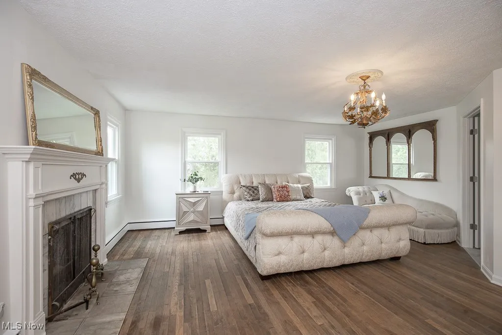 Bedroom with dark wood-type flooring, a chandelier, a fireplace, a textured ceiling, and a baseboard heating unit