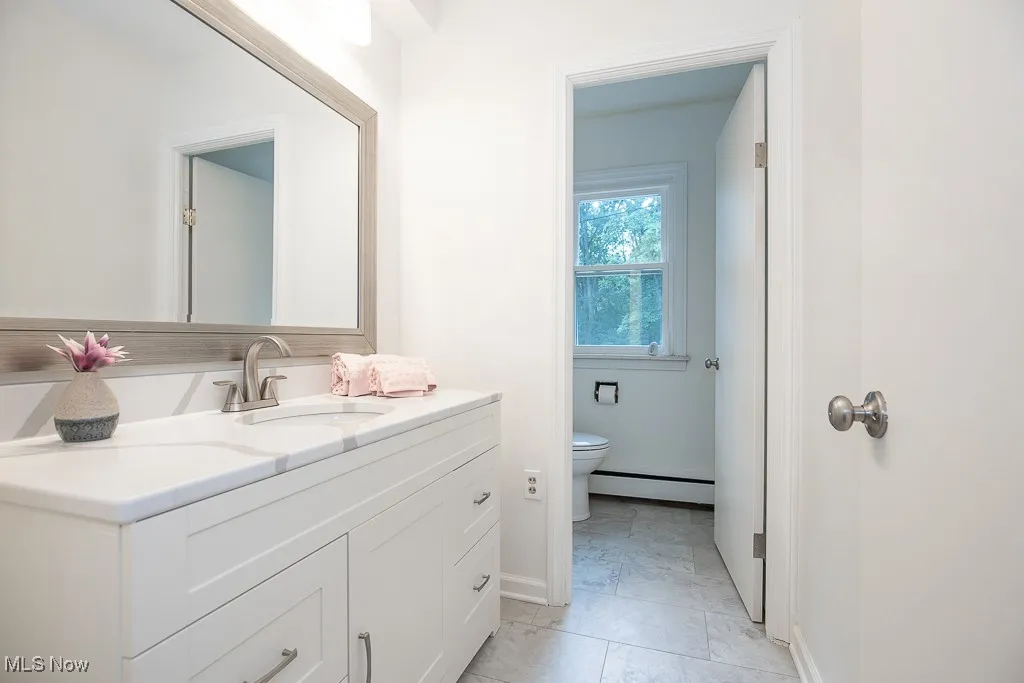 Bathroom with marble finish floors, vanity, and baseboard heating