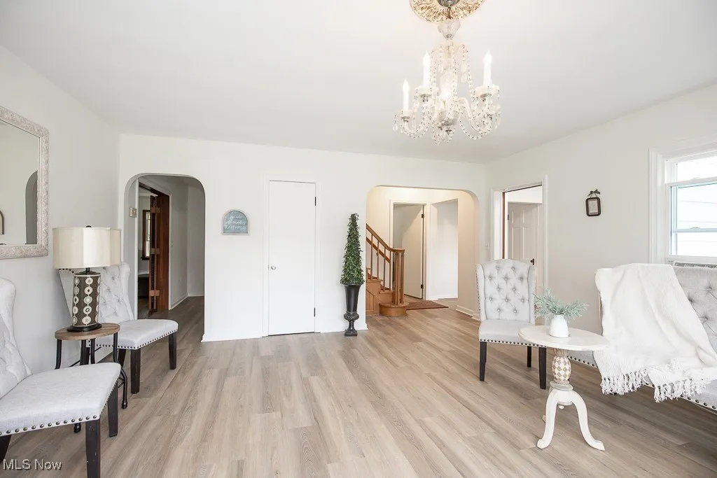 Sitting room featuring arched walkways, light wood finished floors, a chandelier, and stairs