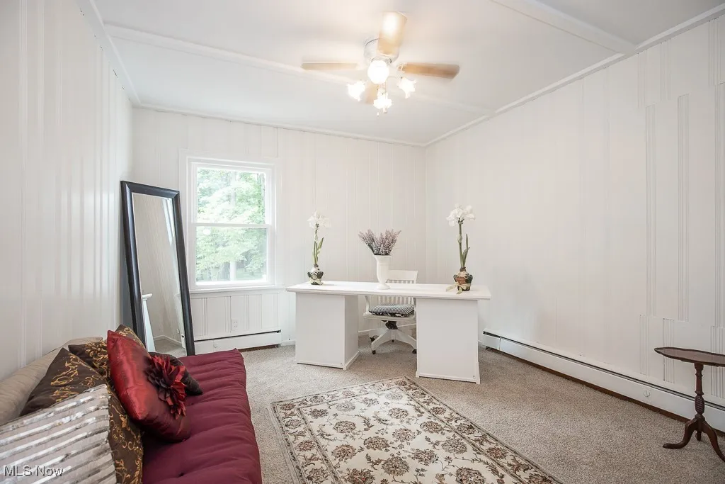 Office area with light colored carpet, a baseboard heating unit, ceiling fan, and ornamental molding