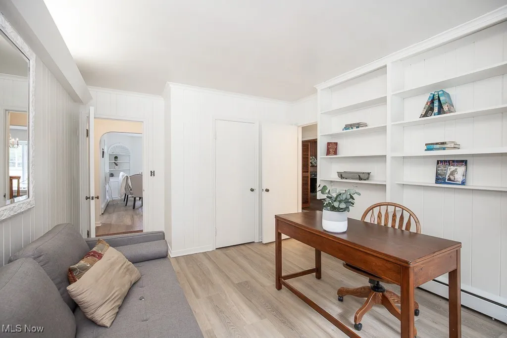 Office with light wood-type flooring, built in shelves, a decorative wall, and crown molding