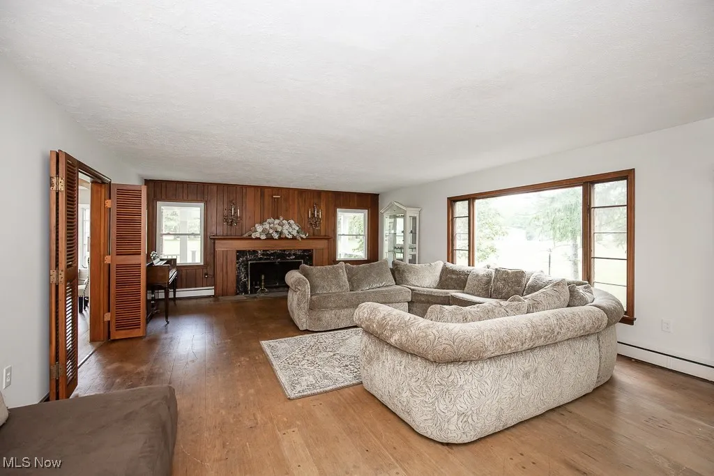 Living room with hardwood / wood-style floors, a fireplace, wood walls, and a baseboard heating unit