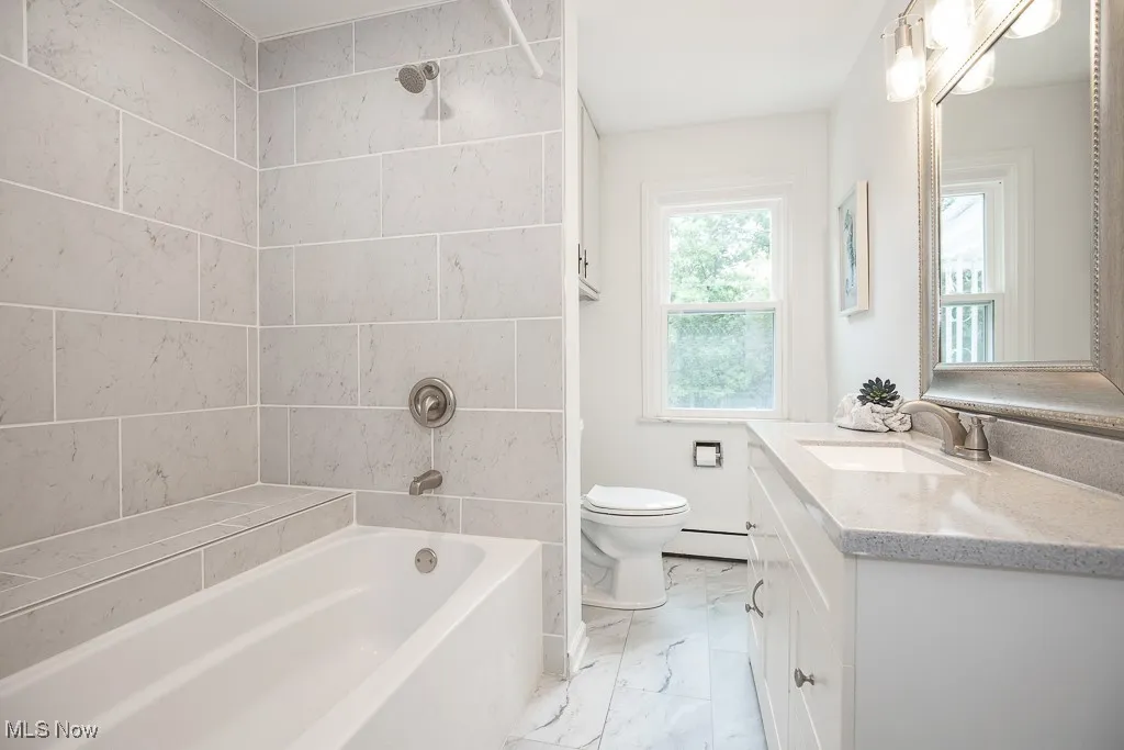 Full bath featuring marble finish floors, vanity, shower / bath combination, and a baseboard heating unit