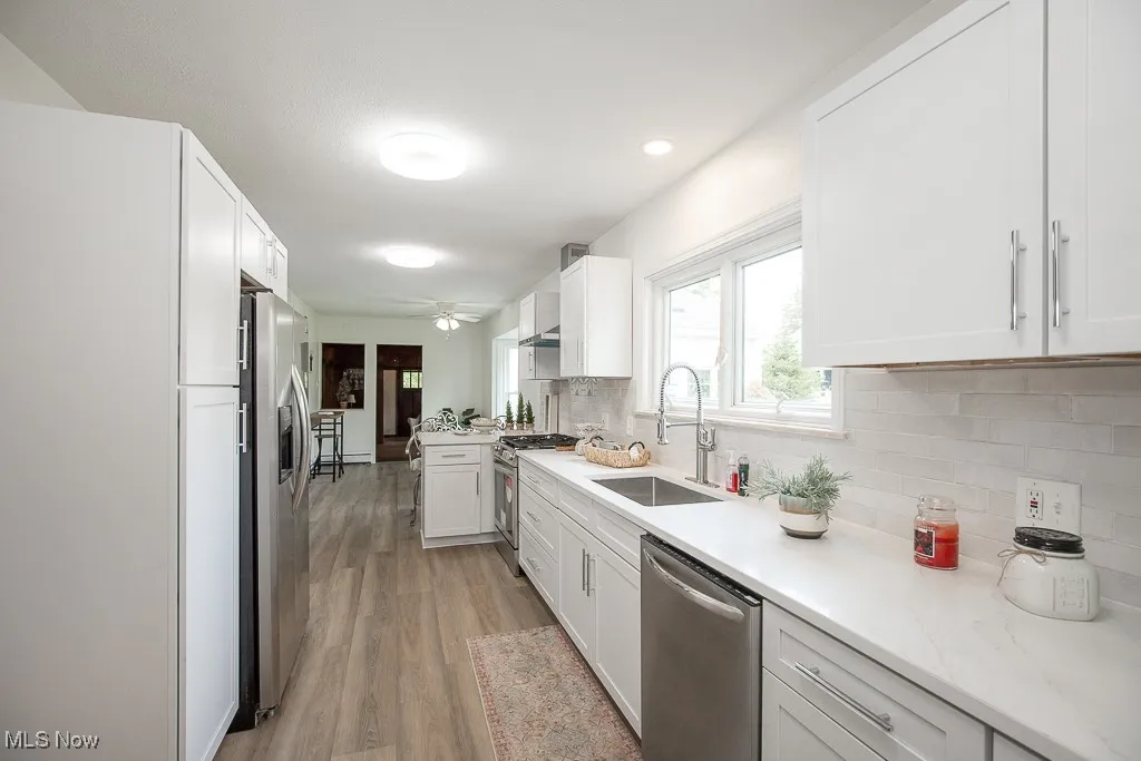 Kitchen with appliances with stainless steel finishes, tasteful backsplash, light wood finished floors, white cabinets, and recessed lighting