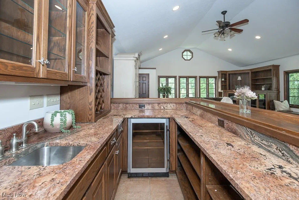 Kitchen featuring wine cooler, recessed lighting, vaulted ceiling, glass insert cabinets, and light stone countertops