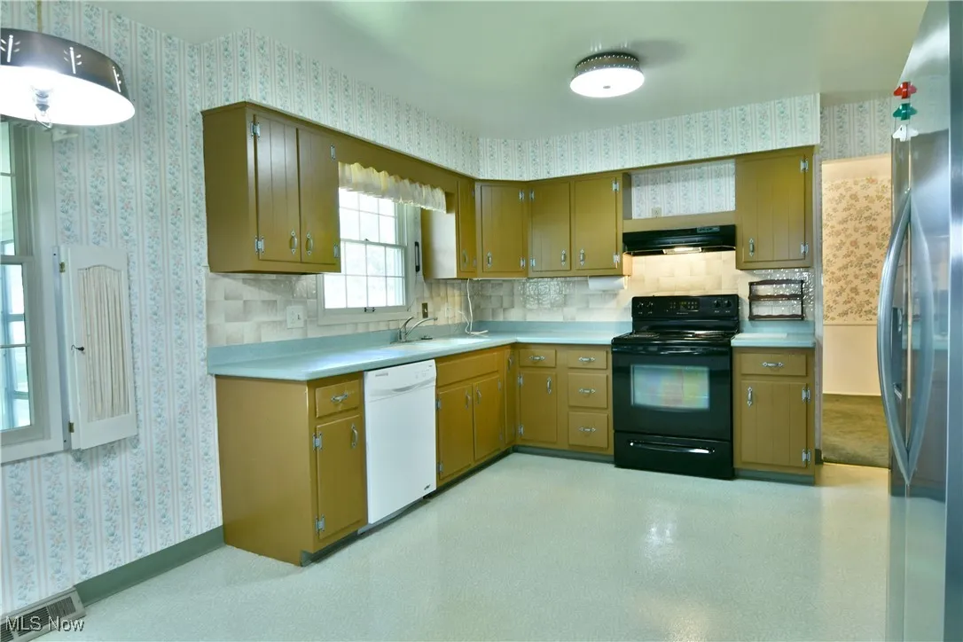 Kitchen featuring black range with electric cooktop, freestanding refrigerator, wallpapered walls, white dishwasher, and light countertops