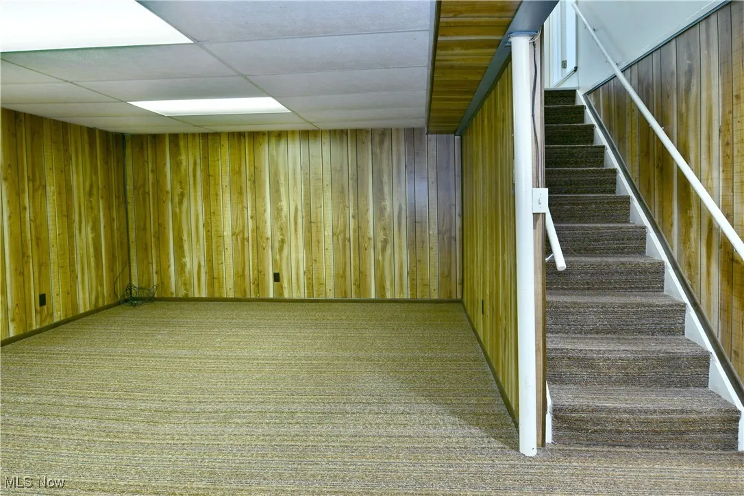 Stairs with carpet floors, wooden walls, and a drop ceiling