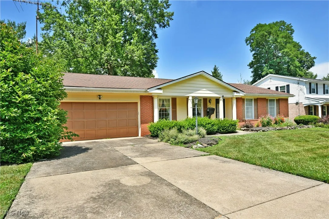 Single story home with concrete driveway, brick siding, an attached garage, a front lawn, and a shingled roof