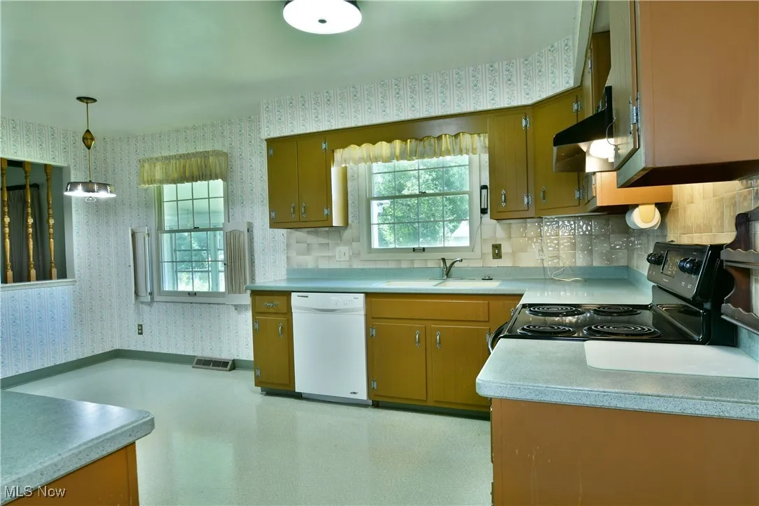 Kitchen with wallpapered walls, black electric range, dishwasher, light countertops, and under cabinet range hood