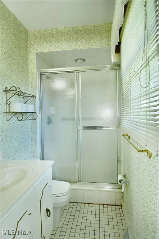 Bathroom with wallpapered walls, a stall shower, tile patterned flooring, and vanity