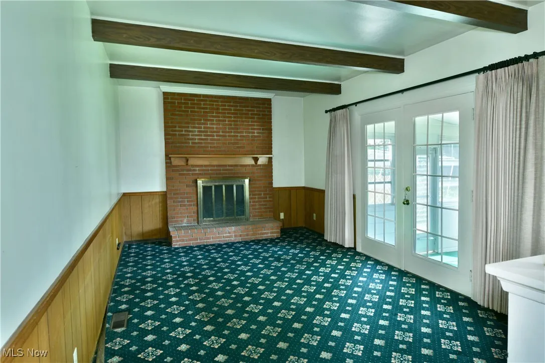 Unfurnished living room featuring a wainscoted wall, beam ceiling, french doors, carpet, and wood walls