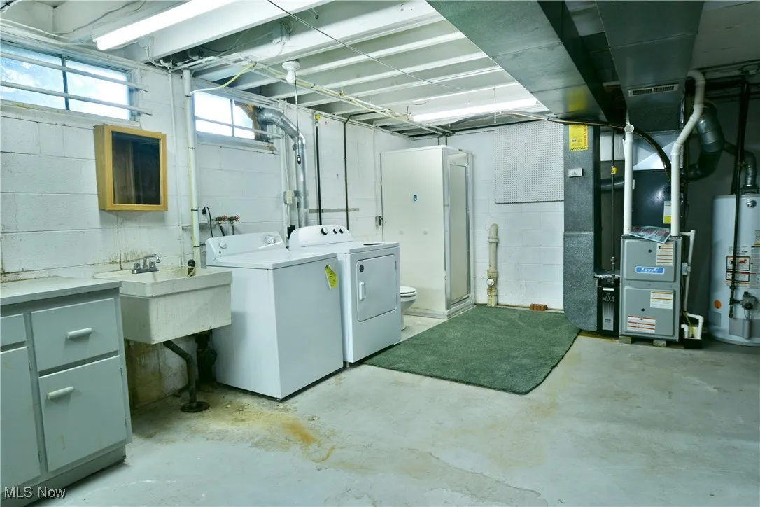 Basement featuring independent washer and dryer, water heater, heating unit, and concrete block wall