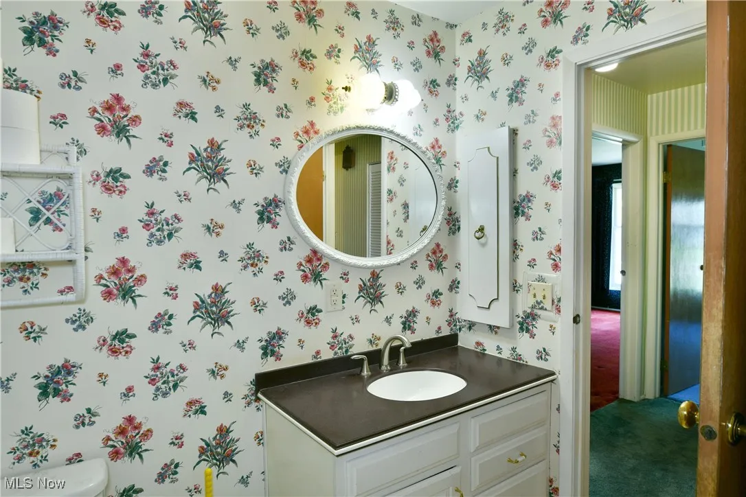 Half bathroom featuring wallpapered walls and vanity