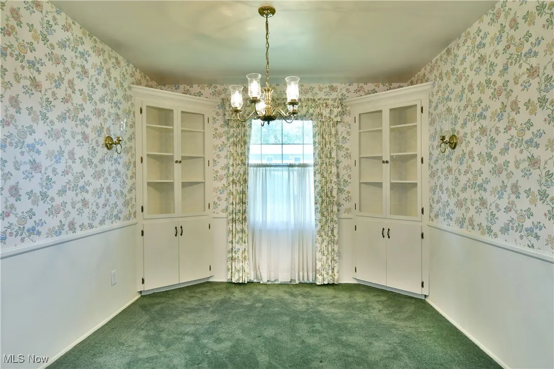 Unfurnished dining area with wallpapered walls, a chandelier, a wainscoted wall, and dark carpet