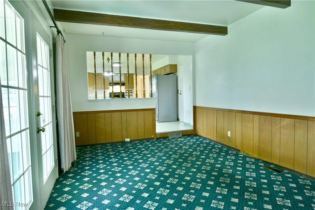 Unfurnished room featuring a wainscoted wall, beamed ceiling, healthy amount of natural light, carpet floors, and wood walls