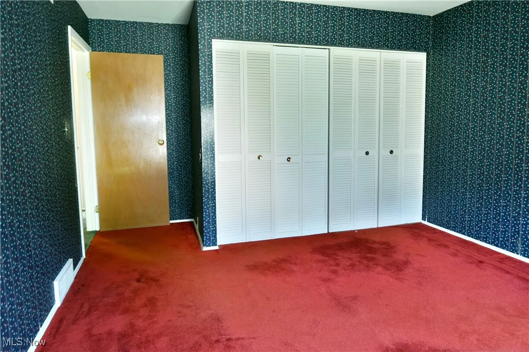 Unfurnished bedroom featuring wallpapered walls, carpet flooring, and a closet