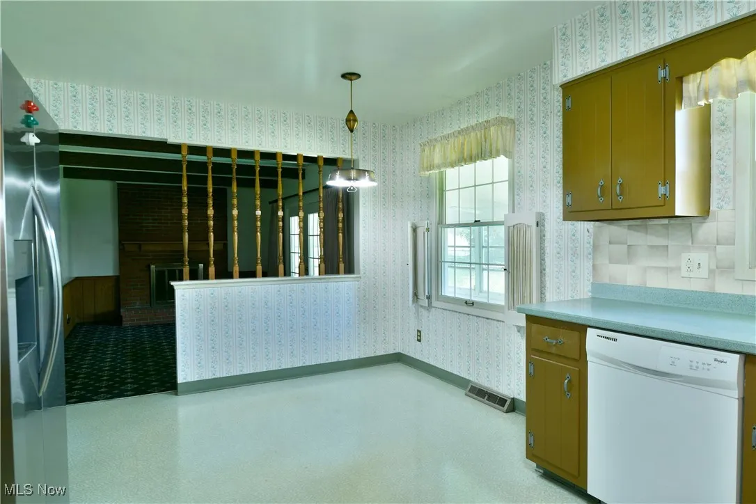 Kitchen with wallpapered walls, white dishwasher, stainless steel refrigerator with ice dispenser, pendant lighting, and light countertops