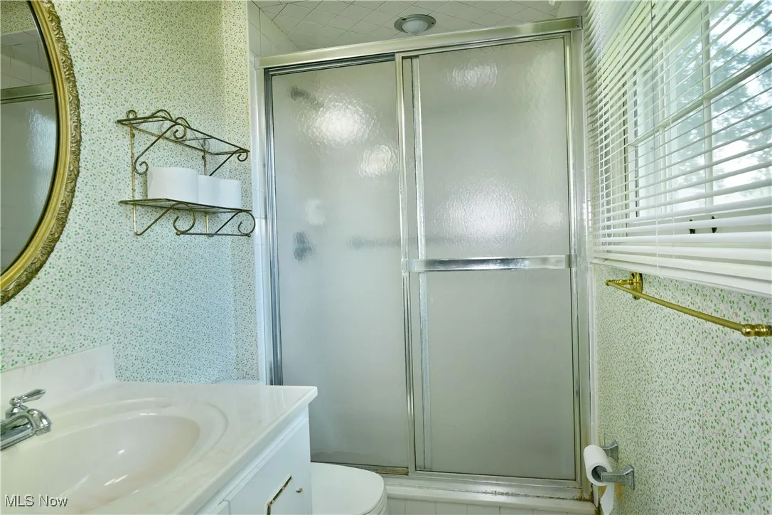 Full bath featuring wallpapered walls, vanity, and a shower stall