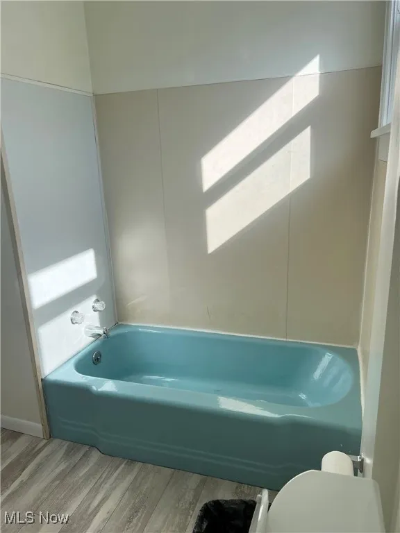 Bathroom with a tub, toilet, vanity, double windows and wood finished floors