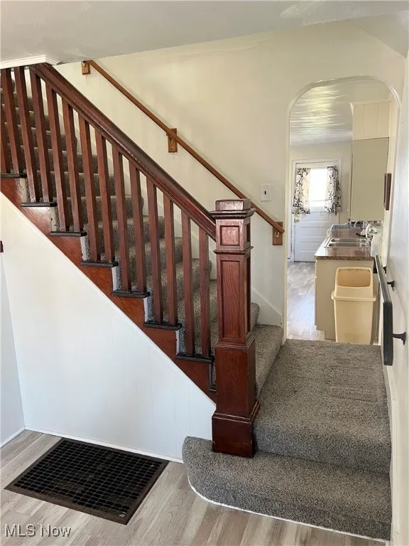 Stairway featuring arched walkways and wood finished floors.