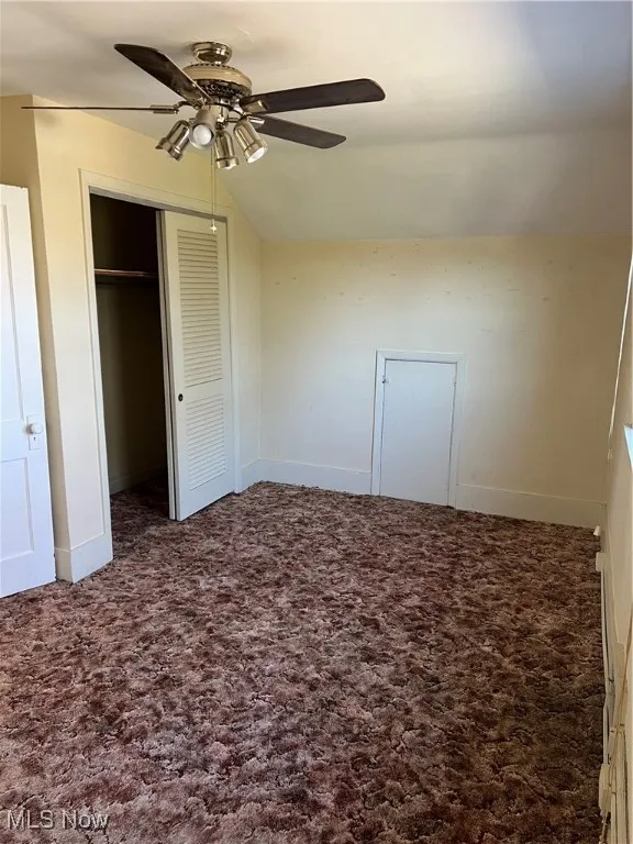Unfurnished bedroom featuring lofted ceiling, carpet, a closet, and baseboards