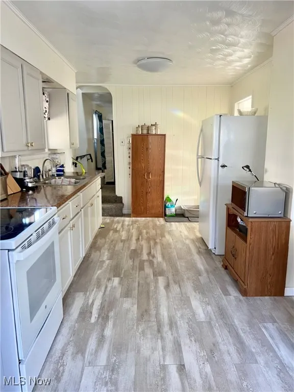 Kitchen featuring white appliances, light wood-style floors, arched walkways, and a sink
