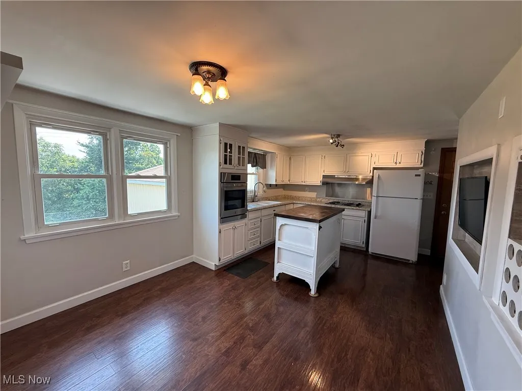 Kitchen featuring appliances with stainless steel finishes, dark wood finished floors, under cabinet range hood, dark countertops, and white cabinetry