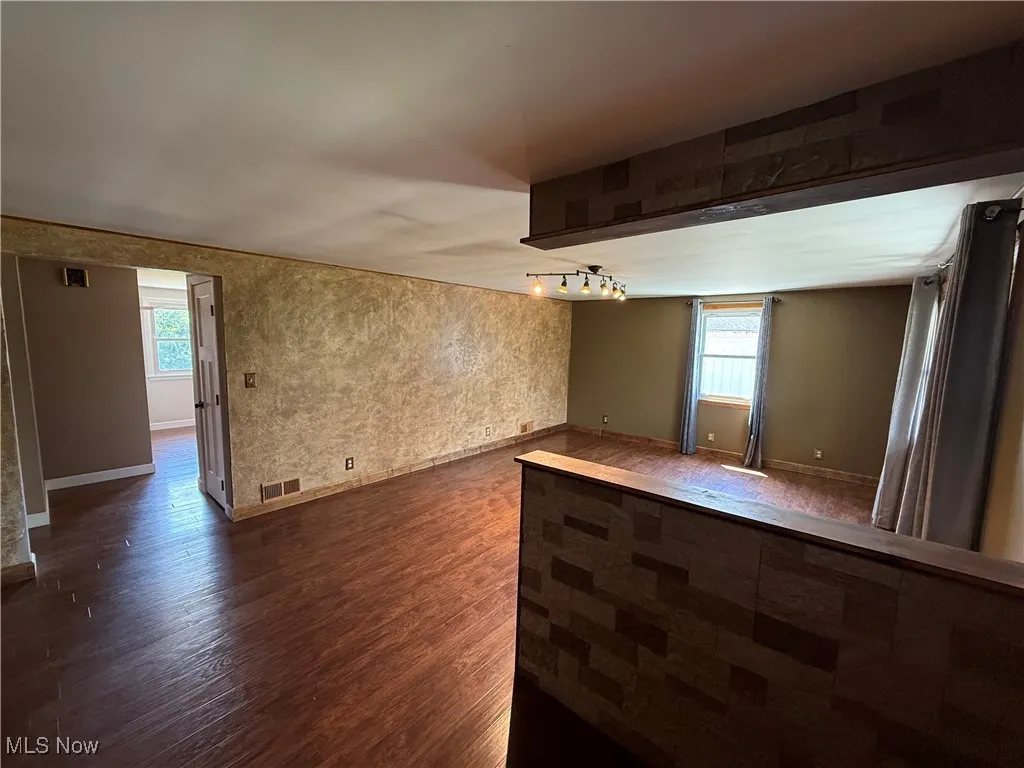 Spare room with dark wood-style flooring, healthy amount of natural light, and bar area