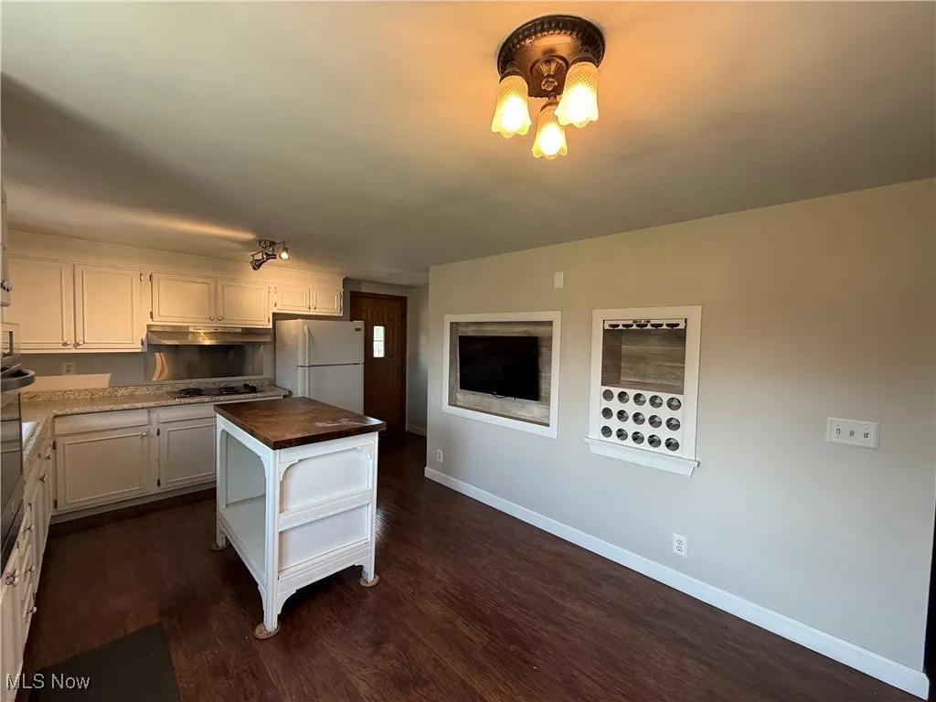 Kitchen featuring freestanding refrigerator, butcher block counters, white cabinetry, dark wood finished floors, and under cabinet range hood