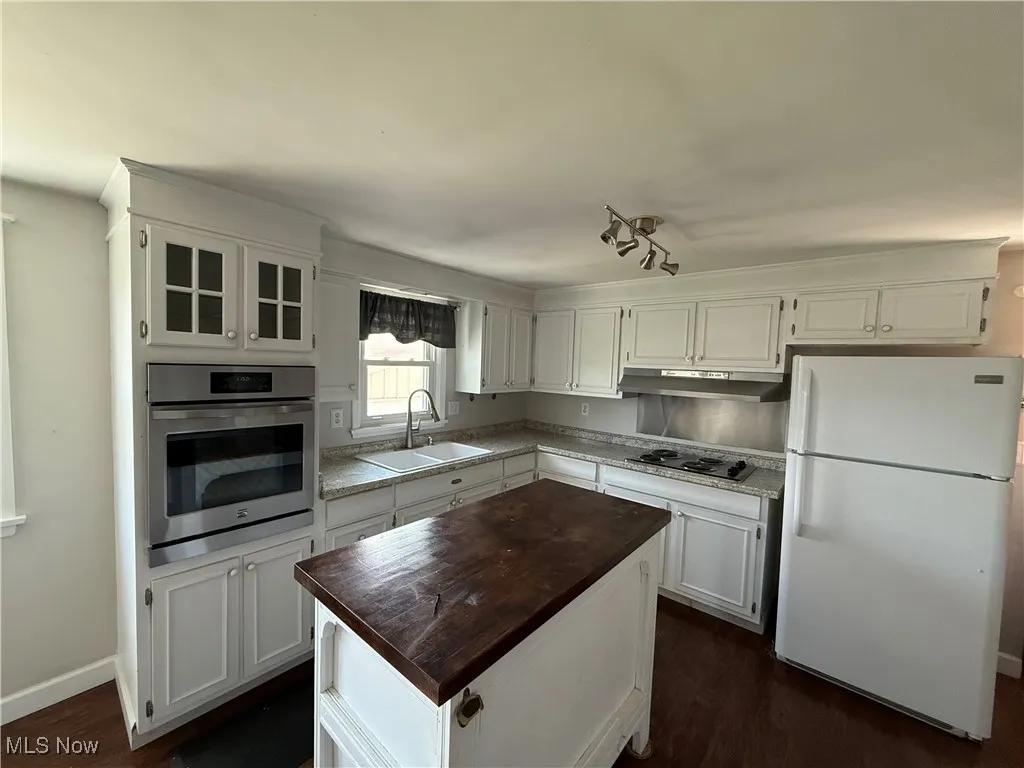 Kitchen with freestanding refrigerator, stainless steel oven, under cabinet range hood, white cabinets, and a center island