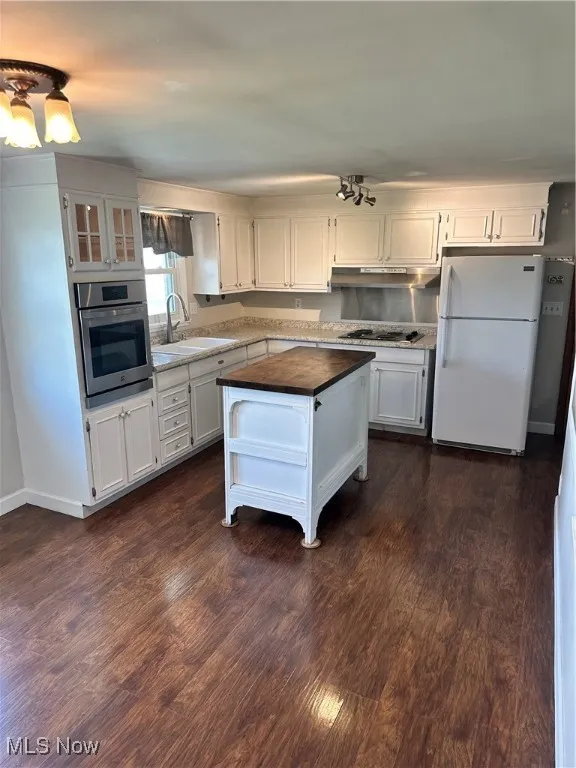 Kitchen with oven, fridge, exhaust hood, white cabinets, and stovetop