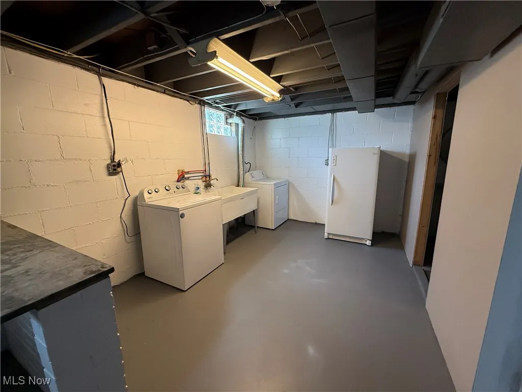 Unfinished below grade area with washing machine and clothes dryer and freestanding refrigerator