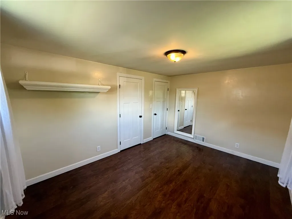 Unfurnished bedroom featuring dark wood finished floors and two closets