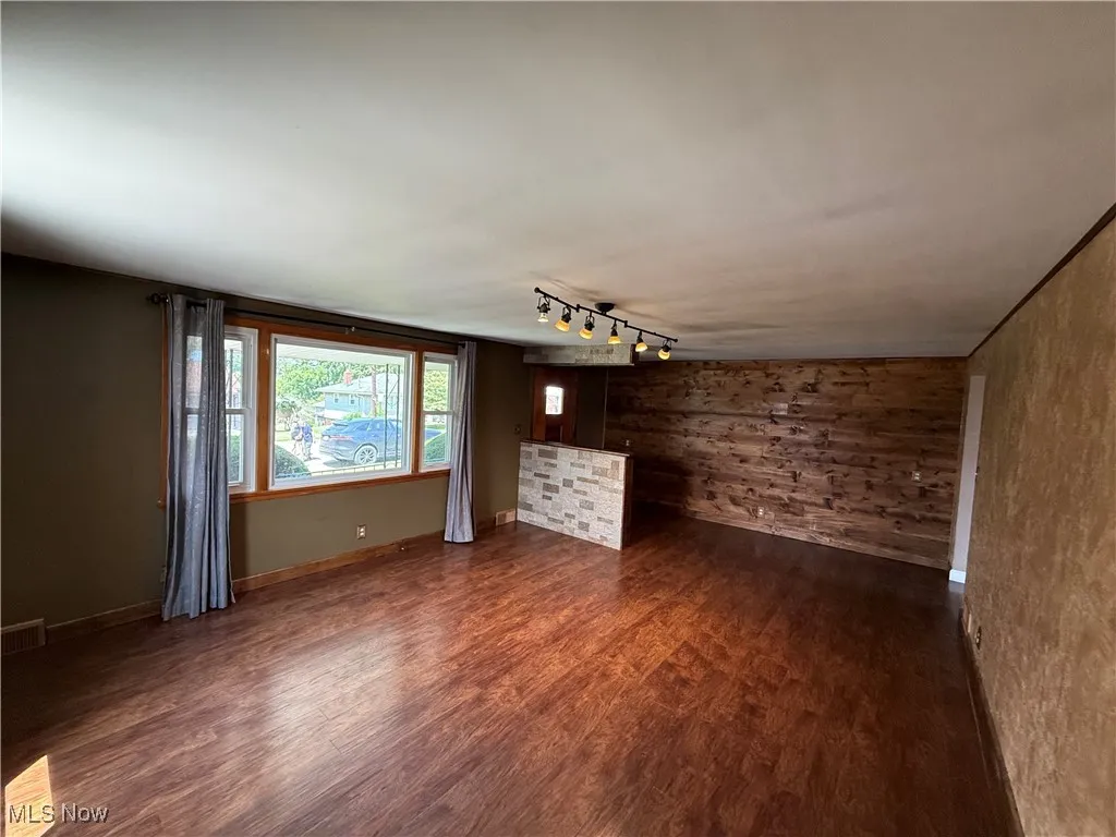 Unfurnished living room with dark wood-style flooring, wooden walls, and track lighting