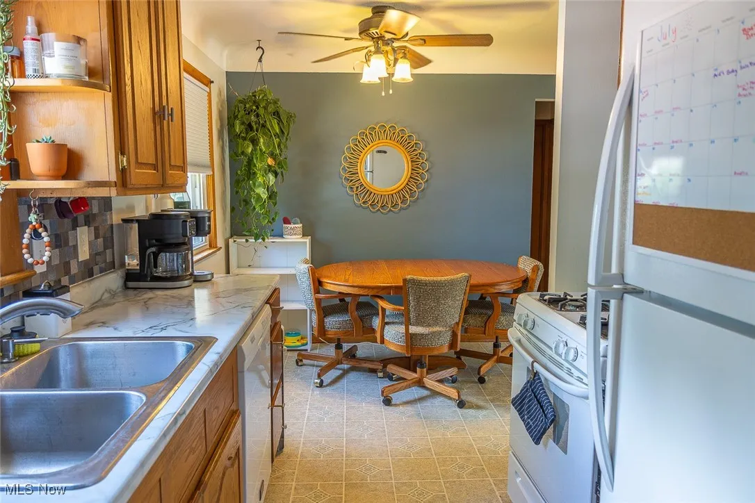Kitchen with white appliances, brown cabinets, ceiling fan, and open shelves
