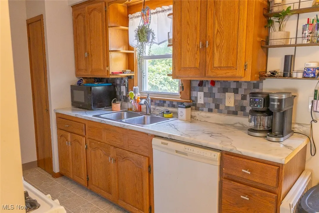 Kitchen with dishwasher, open shelves, black microwave, light countertops, and brown cabinets