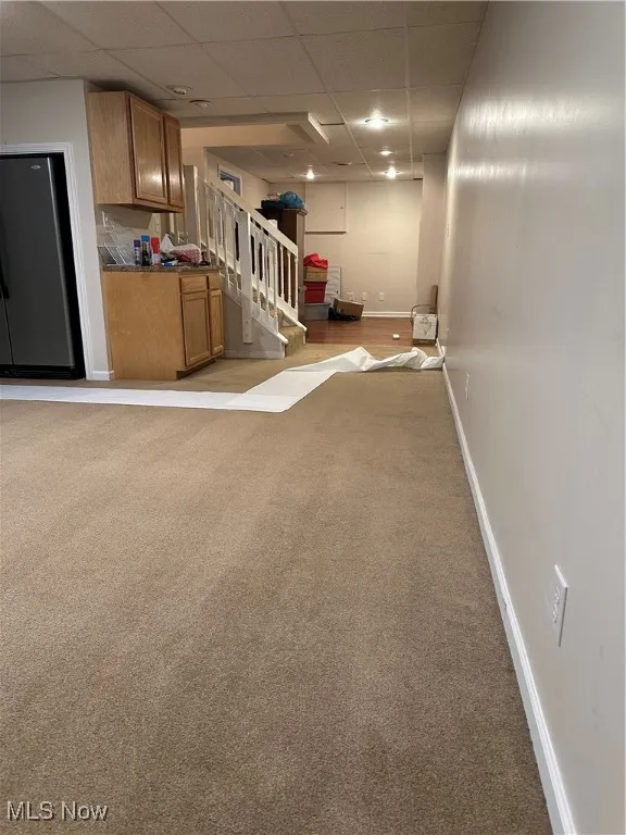 Finished below grade area with a drop ceiling, light carpet, stairs, and fridge