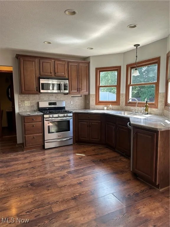 Kitchen featuring stove, dark wood-style floors, backsplash, hanging light fixtures, and a textured ceiling