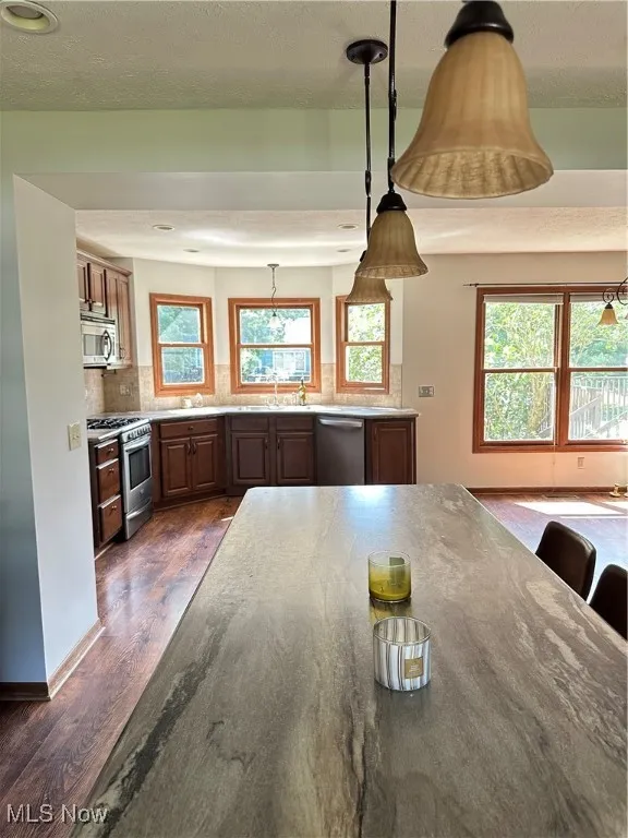 Kitchen featuring dark wood finished floors, decorative backsplash, stove, dishwasher, and hanging light fixtures