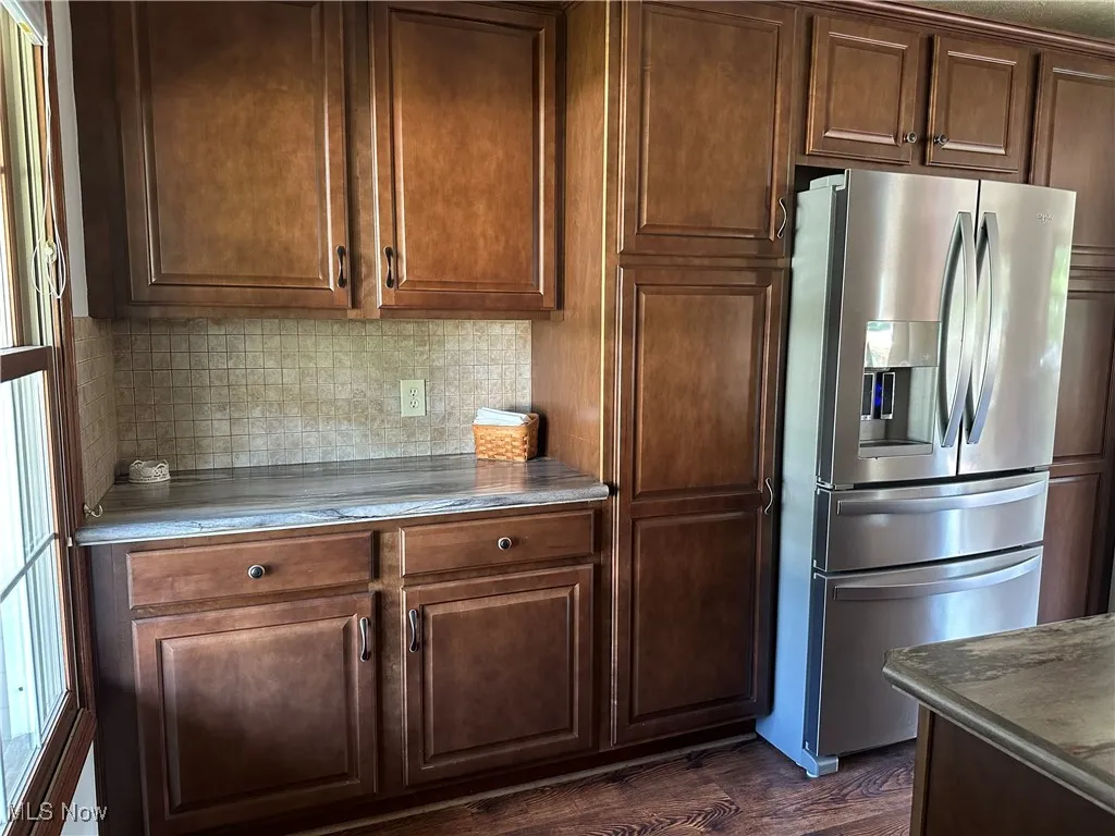 Kitchen featuring stainless steel fridge with ice dispenser, decorative backsplash, and dark wood-style flooring