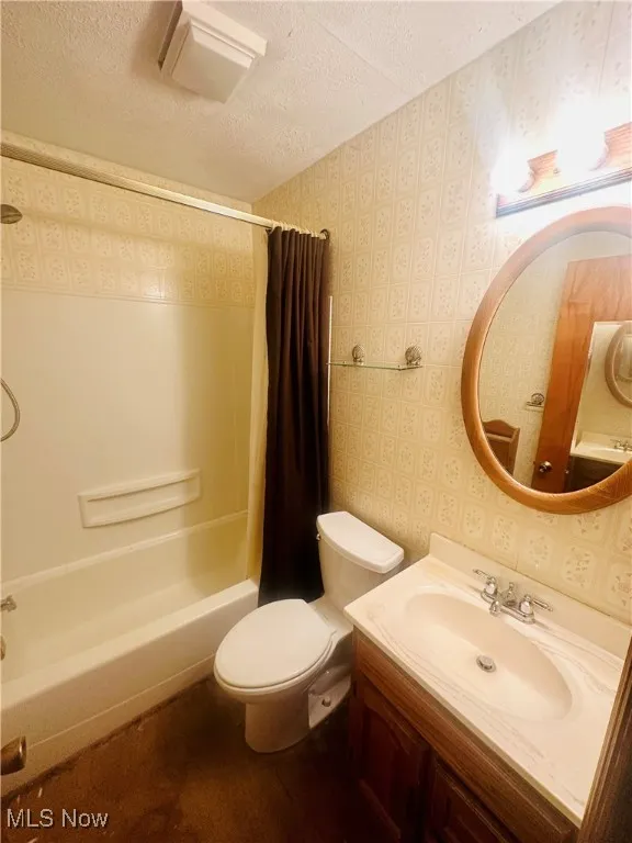 Full bathroom featuring shower / tub combo, vanity, toilet, and a textured ceiling