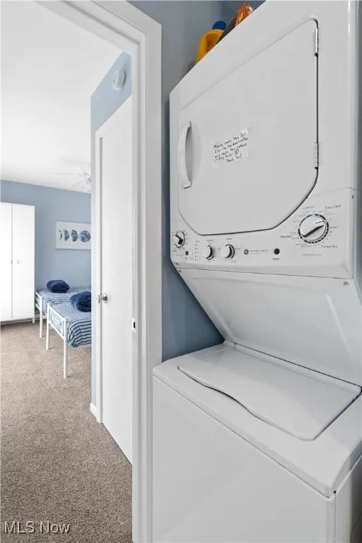Laundry area featuring stacked washer / dryer, carpet flooring, and ceiling fan