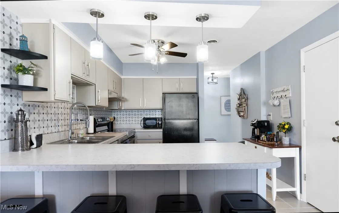 Kitchen with a peninsula, black appliances, light countertops, tasteful backsplash, and open shelves