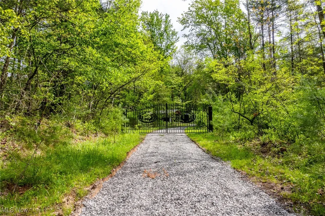 View of dirt / gravel road featuring a gate and a view of trees
