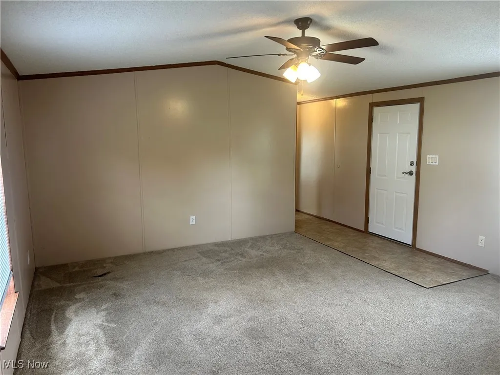 Carpeted spare room with crown molding, a ceiling fan, a textured ceiling, and vaulted ceiling