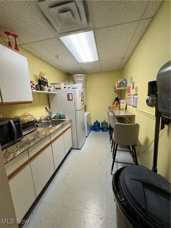 Kitchen featuring a paneled ceiling, white cabinetry, refrigerator, open shelves, and light floors