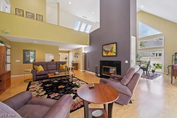 Living room with a towering ceiling, wood finished floors, a fireplace with flush hearth, and recessed lighting