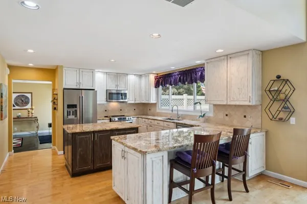 Kitchen featuring stainless steel appliances, recessed lighting, light stone counters, tasteful backsplash, and a peninsula