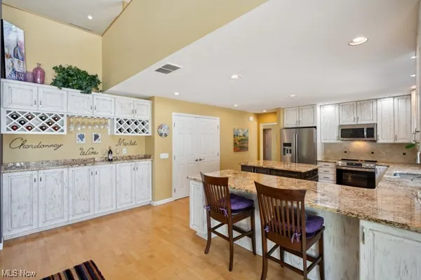 Kitchen featuring appliances with stainless steel finishes, light stone counters, a kitchen island, backsplash, and recessed lighting