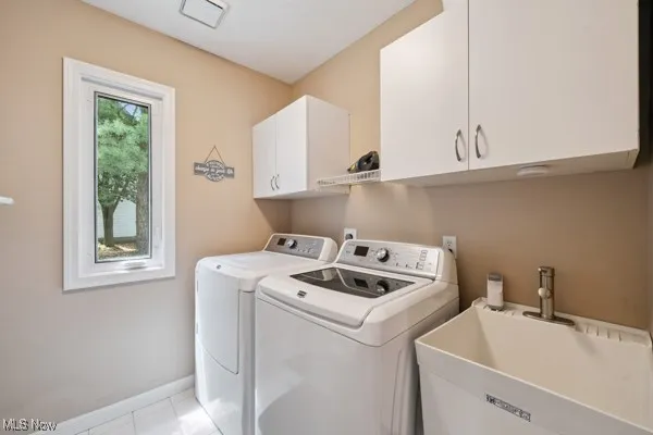 Washroom with cabinet space, washer and dryer, and light tile patterned floors